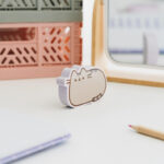 Gumka do zmazywania w kształcie kotki Pusheen ustawiona na biurku przy oknie.